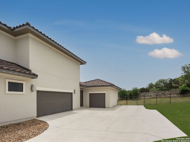 view of property exterior with fence, stucco siding, driveway, and a tiled roof