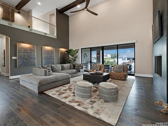 living area featuring beamed ceiling, a towering ceiling, ceiling fan, and dark wood-type flooring