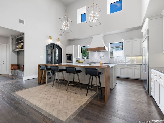 kitchen featuring an inviting chandelier, visible vents, custom range hood, and a high ceiling