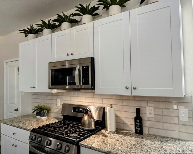 kitchen featuring light stone counters, white cabinetry, stainless steel appliances, and backsplash