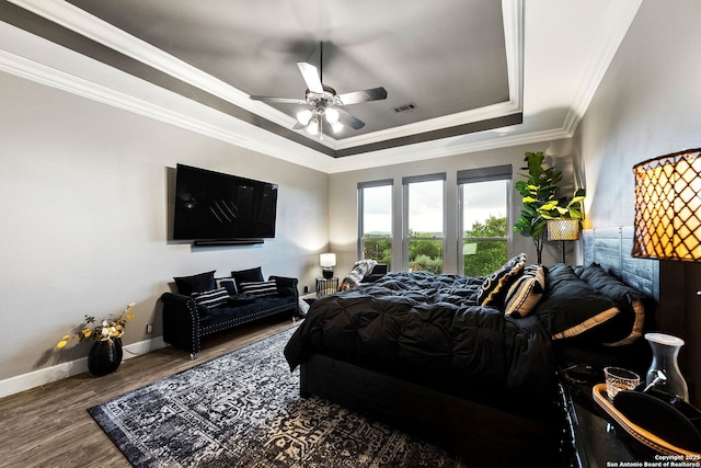 bedroom featuring wood finished floors, baseboards, visible vents, crown molding, and a tray ceiling