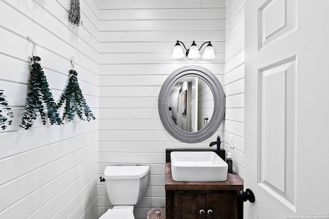 bathroom featuring wood walls, toilet, and vanity