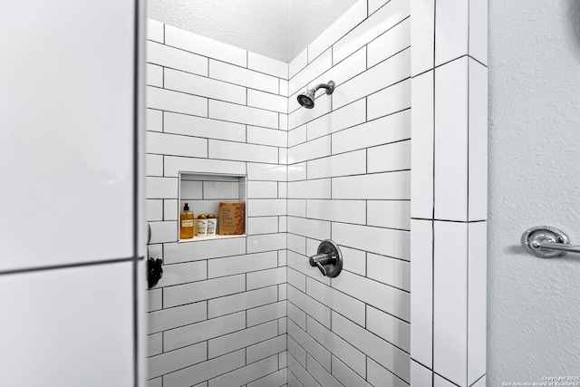 bathroom with a textured wall and tiled shower
