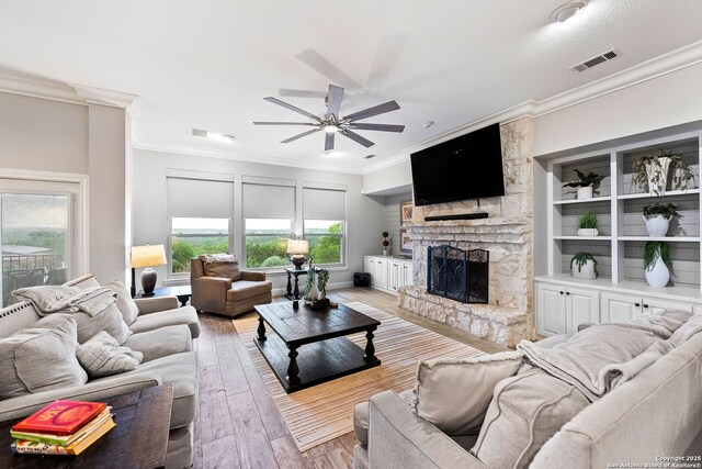 living room with ornamental molding, ceiling fan, a stone fireplace, light wood finished floors, and visible vents