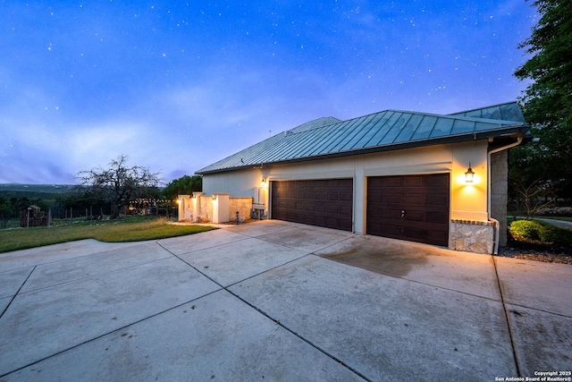 view of front of property with a standing seam roof, a front yard, metal roof, driveway, and stone siding