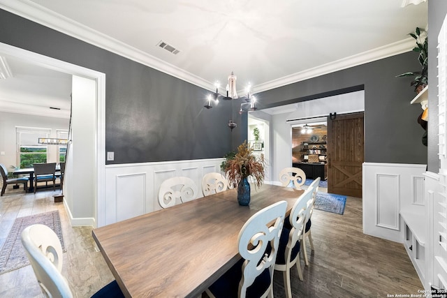 dining room with visible vents, a barn door, ornamental molding, and a decorative wall