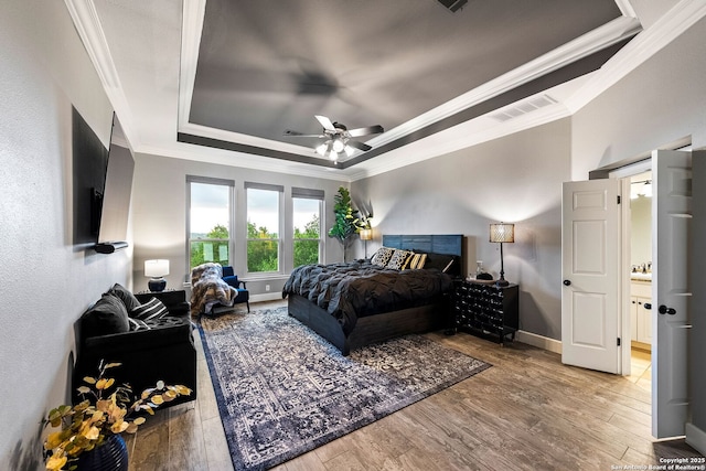 bedroom with wood finished floors, ornamental molding, baseboards, visible vents, and a raised ceiling