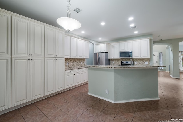 kitchen with tile patterned flooring, arched walkways, backsplash, and appliances with stainless steel finishes