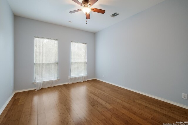 empty room featuring wood finished floors, visible vents, a ceiling fan, and baseboards