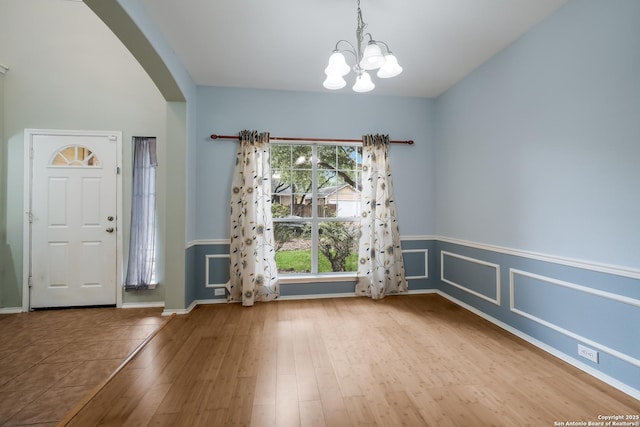 interior space with an inviting chandelier, wood finished floors, baseboards, and arched walkways