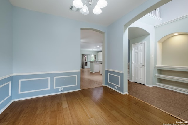 unfurnished room with wood finished floors, visible vents, a notable chandelier, and arched walkways