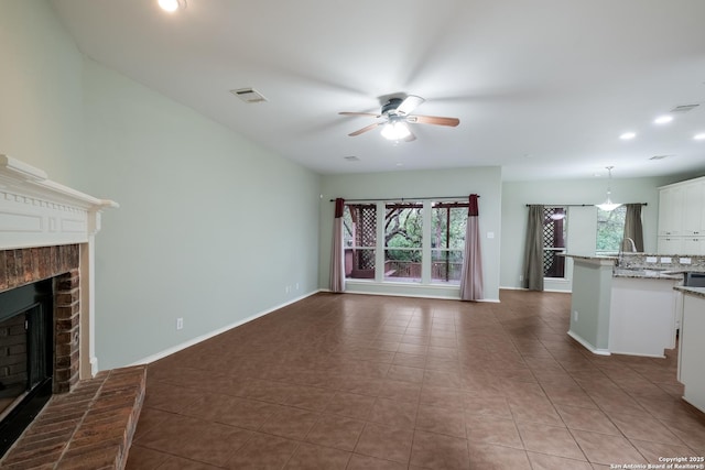 unfurnished living room with a fireplace, a ceiling fan, visible vents, and plenty of natural light