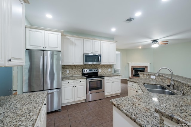 kitchen with a sink, a fireplace, tasteful backsplash, a ceiling fan, and appliances with stainless steel finishes