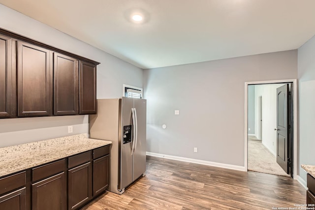 kitchen with light stone counters, light wood-style floors, dark brown cabinetry, baseboards, and stainless steel fridge with ice dispenser