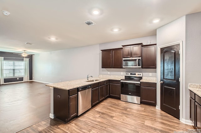 kitchen with a sink, stainless steel appliances, dark brown cabinets, light wood-type flooring, and a peninsula