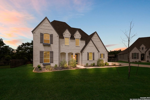 french country style house featuring brick siding, fence, and a lawn