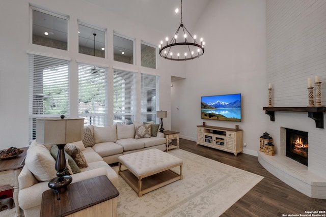 living area featuring an inviting chandelier, a fireplace, high vaulted ceiling, baseboards, and wood finished floors