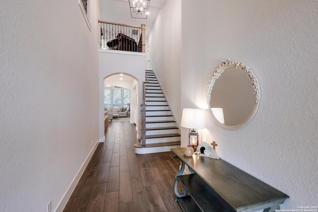 hall featuring dark wood finished floors, arched walkways, a chandelier, baseboards, and stairway