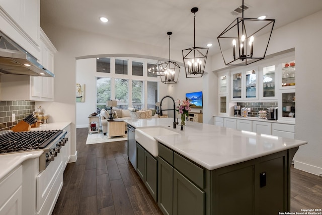 kitchen with stainless steel dishwasher, under cabinet range hood, a sink, visible vents, and a notable chandelier