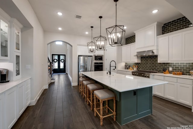kitchen featuring wall chimney range hood, a kitchen breakfast bar, tasteful backsplash, appliances with stainless steel finishes, and arched walkways