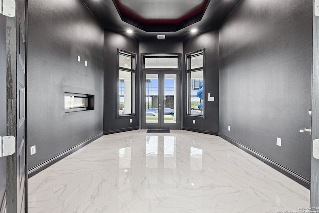 foyer with french doors, baseboards, a raised ceiling, marble finish floor, and a high ceiling