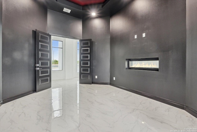 empty room featuring a high ceiling, a glass covered fireplace, baseboards, and marble finish floor