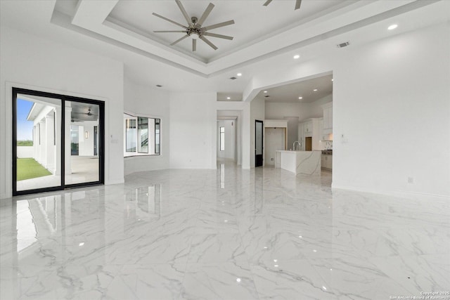 unfurnished living room with recessed lighting, marble finish floor, ceiling fan, and a tray ceiling