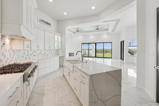 kitchen with marble finish floor, stainless steel gas cooktop, light stone countertops, ceiling fan, and a sink