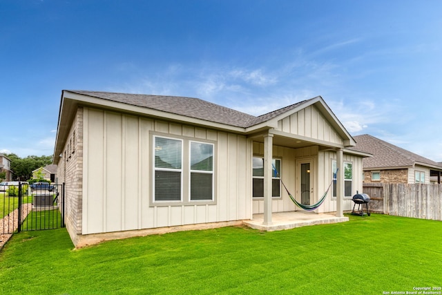 back of property featuring a patio area, a fenced backyard, a lawn, board and batten siding, and roof with shingles
