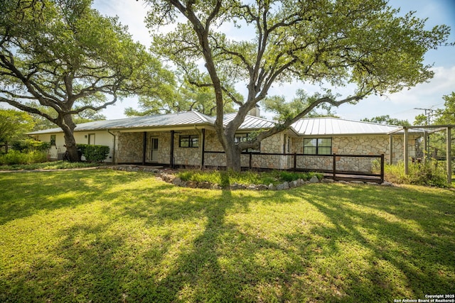 back of house featuring metal roof, a standing seam roof, a yard, and stone siding