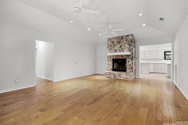 unfurnished living room featuring a stone fireplace, light wood finished floors, visible vents, a ceiling fan, and lofted ceiling