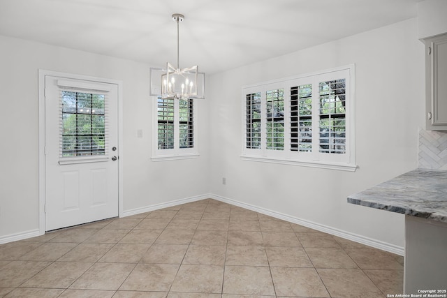 unfurnished dining area with light tile patterned floors, an inviting chandelier, and baseboards