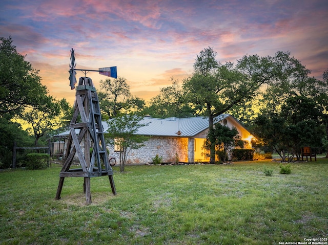 back of house at dusk featuring stone siding, metal roof, and a lawn