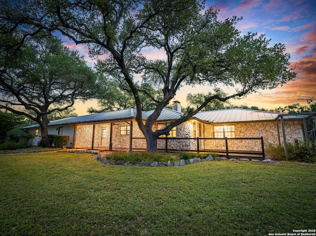 rear view of property with a standing seam roof, metal roof, a lawn, stone siding, and a chimney