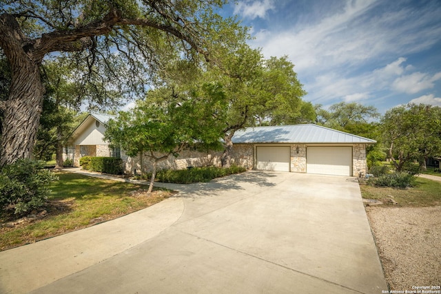 view of front of property with driveway, a garage, metal roof, and stone siding