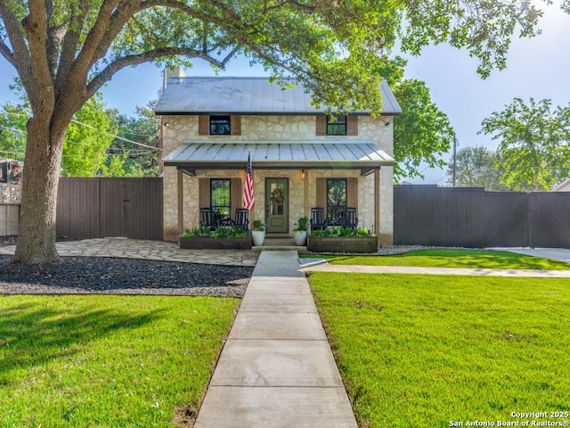 view of front of property featuring a porch, a standing seam roof, a front yard, stone siding, and fence