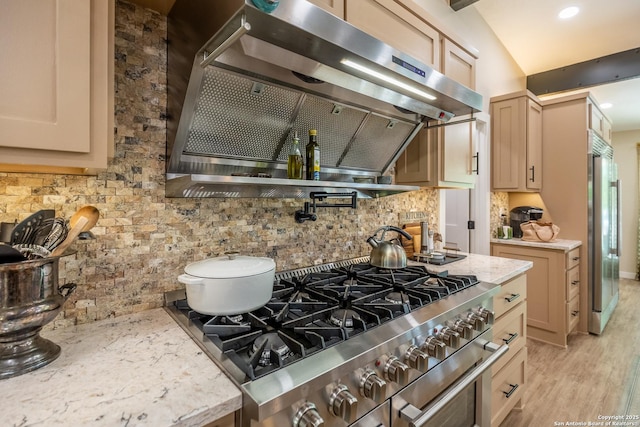 kitchen featuring tasteful backsplash, light wood-style floors, stainless steel gas range, light stone countertops, and range hood