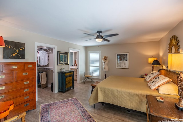 bedroom with a closet, ceiling fan, a walk in closet, baseboards, and wood finished floors
