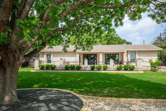 ranch-style house with a front lawn, fence, roof with shingles, and brick siding