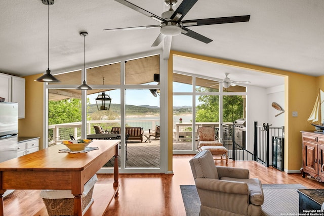 living area with floor to ceiling windows, ceiling fan, light wood-style flooring, and vaulted ceiling
