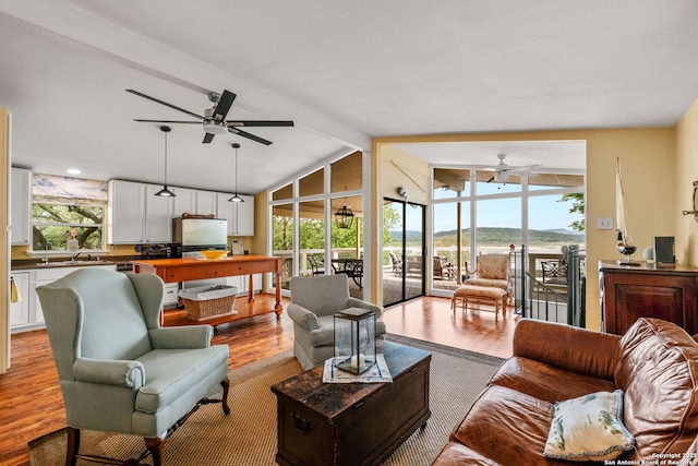 living room with a wall of windows, wood finished floors, lofted ceiling with beams, and a ceiling fan