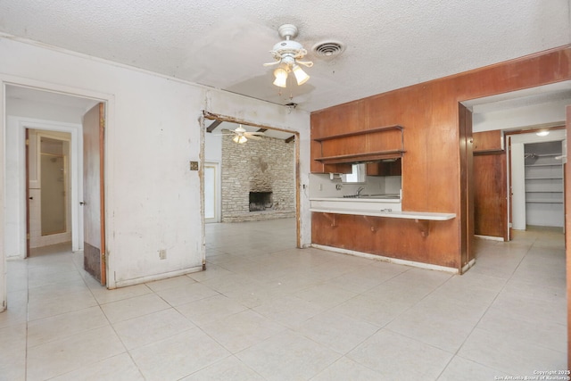unfurnished living room with a fireplace, a textured ceiling, ceiling fan, and wooden walls