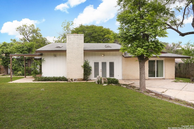 back of property featuring a chimney, brick siding, fence, french doors, and a lawn