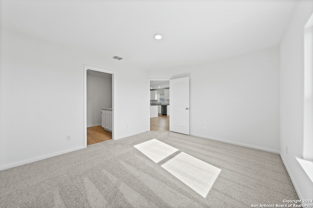 unfurnished bedroom with recessed lighting, ensuite bath, visible vents, baseboards, and light colored carpet