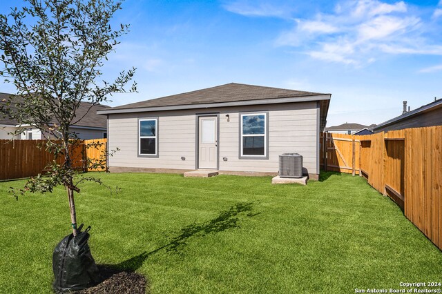 back of house with a shingled roof, a fenced backyard, central AC unit, and a lawn