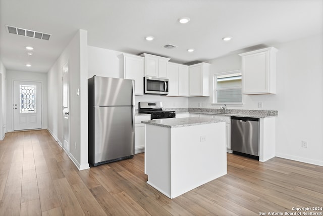 kitchen featuring light wood-style flooring, appliances with stainless steel finishes, white cabinets, a center island, and visible vents