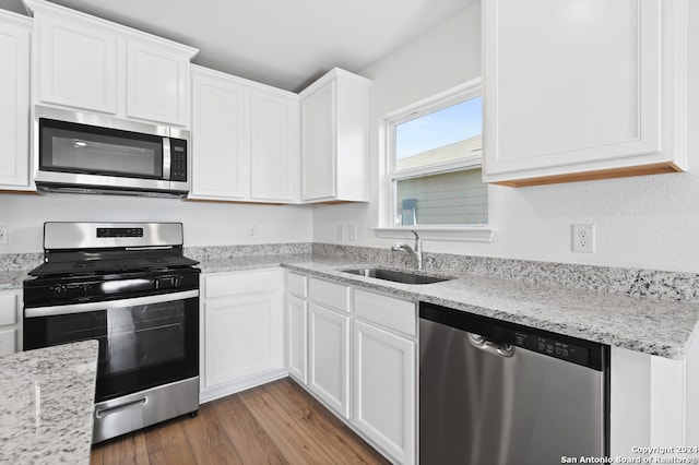 kitchen with light stone countertops, a sink, light wood-style flooring, white cabinets, and appliances with stainless steel finishes