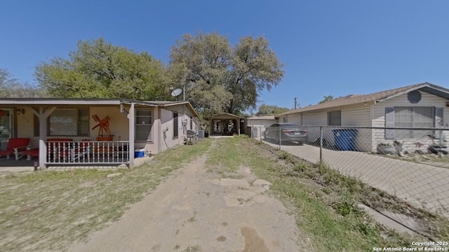 view of side of property featuring a porch, fence, a carport, and dirt driveway