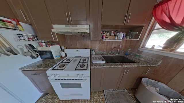 kitchen featuring open shelves, a sink, under cabinet range hood, gas range gas stove, and light stone countertops