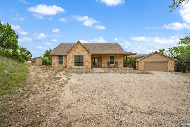 single story home featuring a porch, dirt driveway, a garage, brick siding, and an outdoor structure